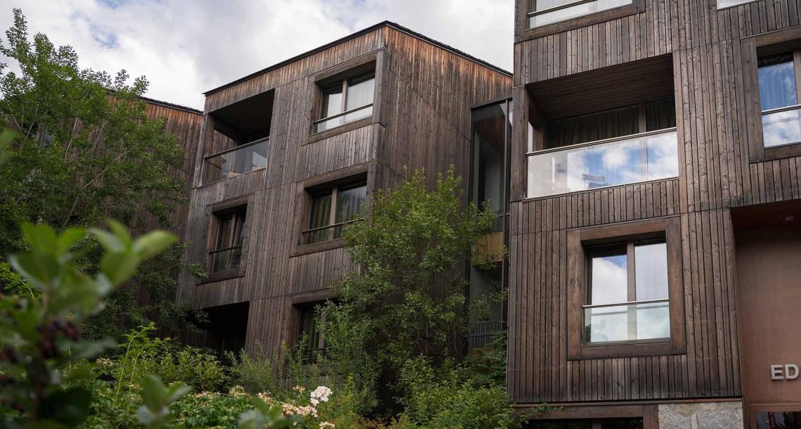 Edificio moderno in legno con ampie finestre e vegetazione circostante.