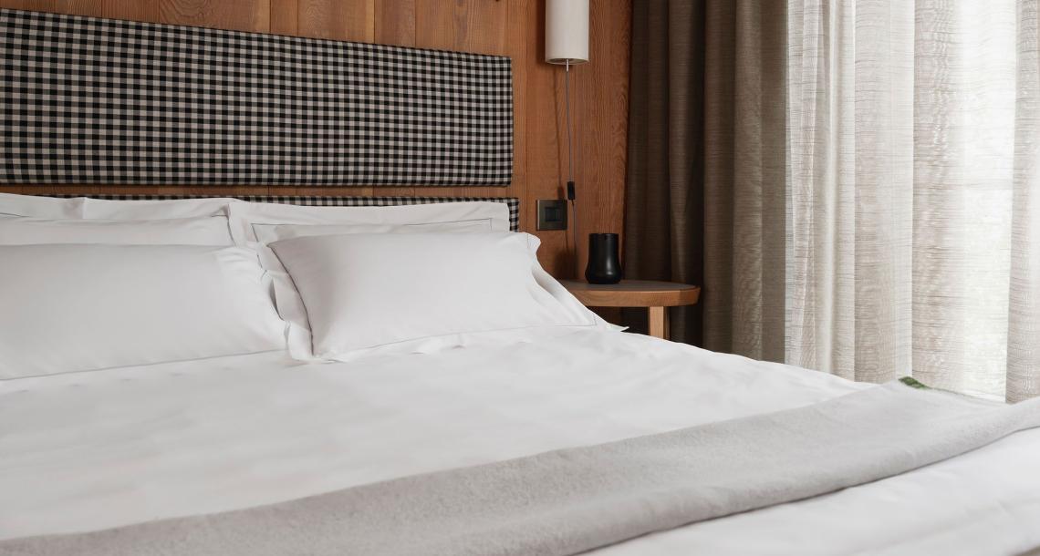 Camera da letto moderna con letto bianco, testiera a quadri e tende beige.