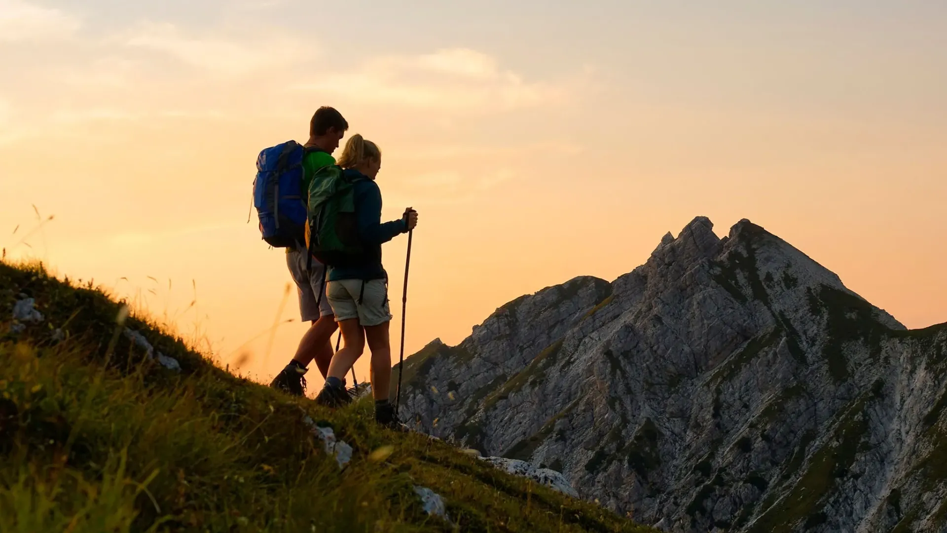 Due escursionisti camminano al tramonto su un sentiero di montagna.