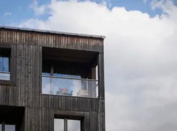 Edificio moderno in legno con balcone, cielo parzialmente nuvoloso sullo sfondo.