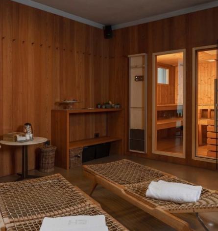 Sala relax con lettini in legno e sauna adiacente, atmosfera accogliente.