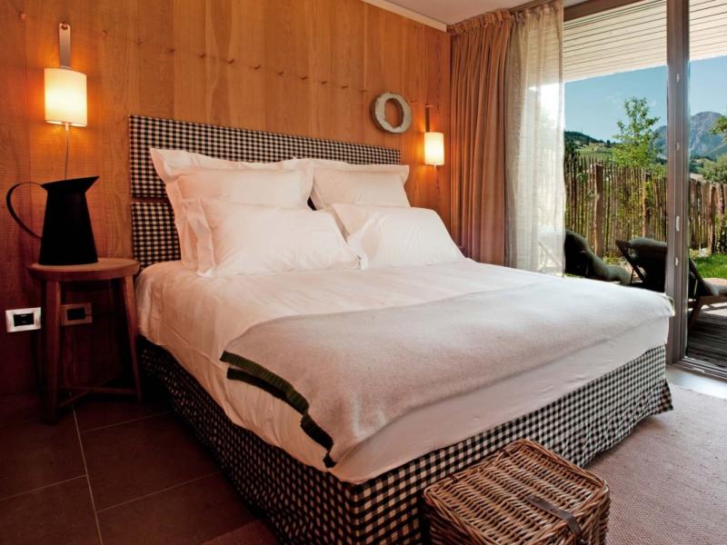 Camera da letto accogliente con vista sul giardino e montagne, arredi in legno e tessuti.