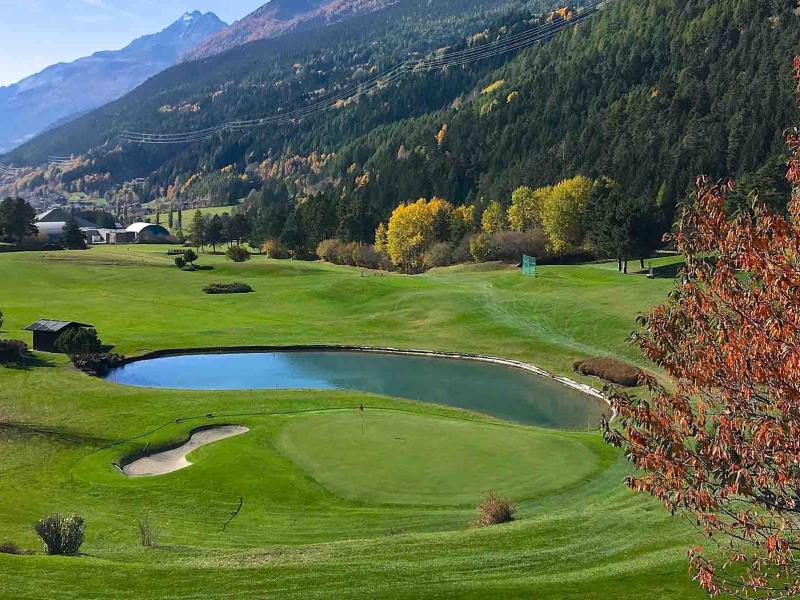 Campo da golf immerso nella natura con montagne e laghetto.