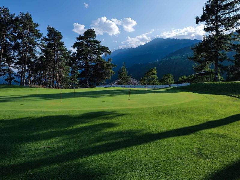 Campo da golf verde con alberi e montagne sullo sfondo.
