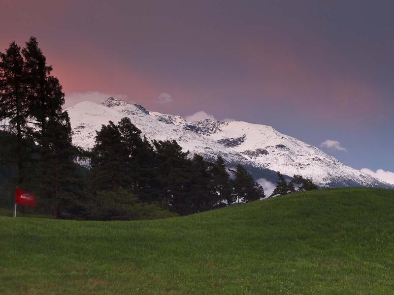 Prato verde, bandiera rossa, montagne innevate e cielo al tramonto.