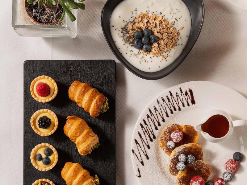 Colazione con yogurt, dolci, frutta, succo d'arancia e pane su tavola apparecchiata.