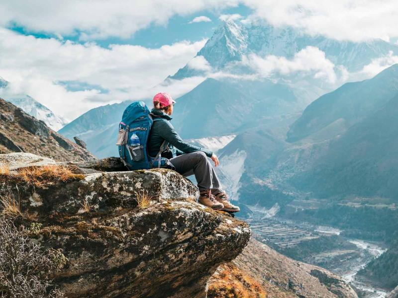 Escursionista seduto su una roccia, ammirando le montagne innevate e la valle sottostante.